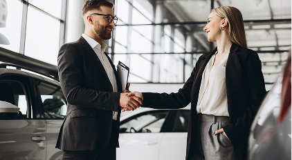Man and woman shaking hands in a car dealership with cars in the background.