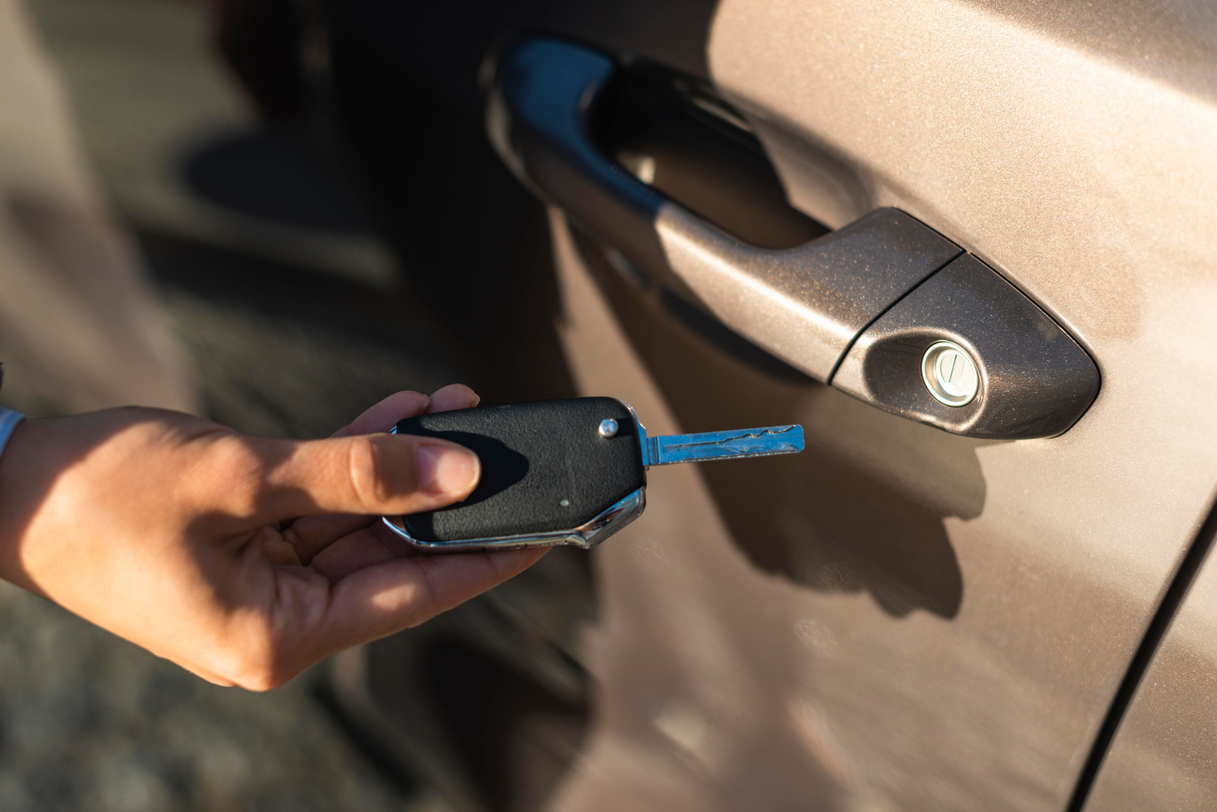 Hand holding car key near car door handle.